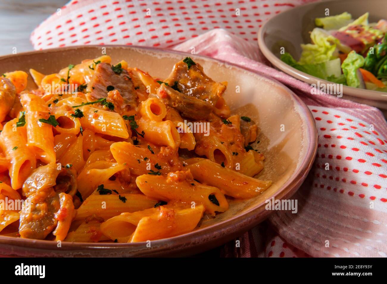 Italian penne alla vodka pink cream sauce with sliced spicy sausage and side salad Stock Photo