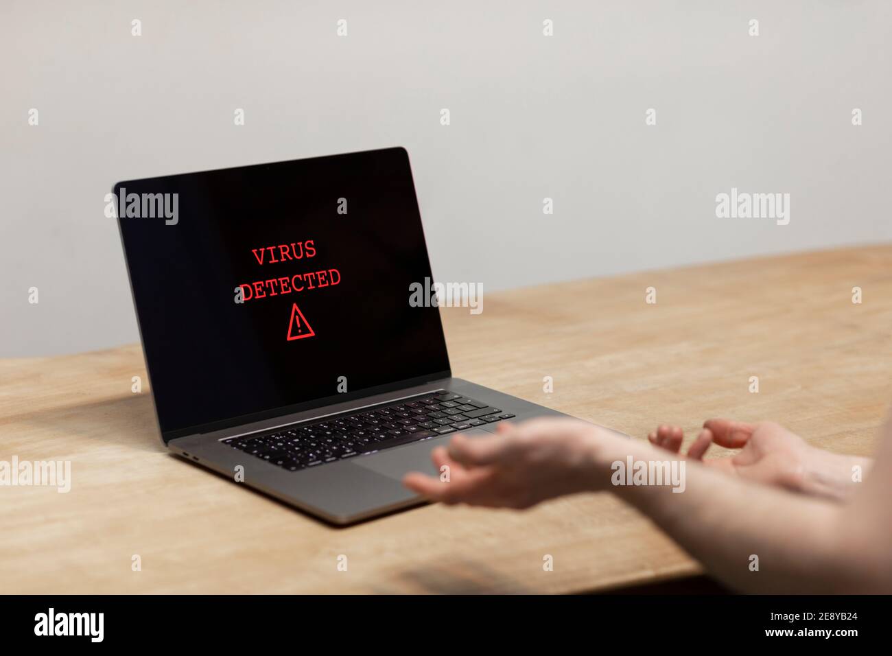 Virus detected on a laptop. A desperate man holding his hands up towards the computer with the warning on his screen. Cybercrime, malware, infected un Stock Photo