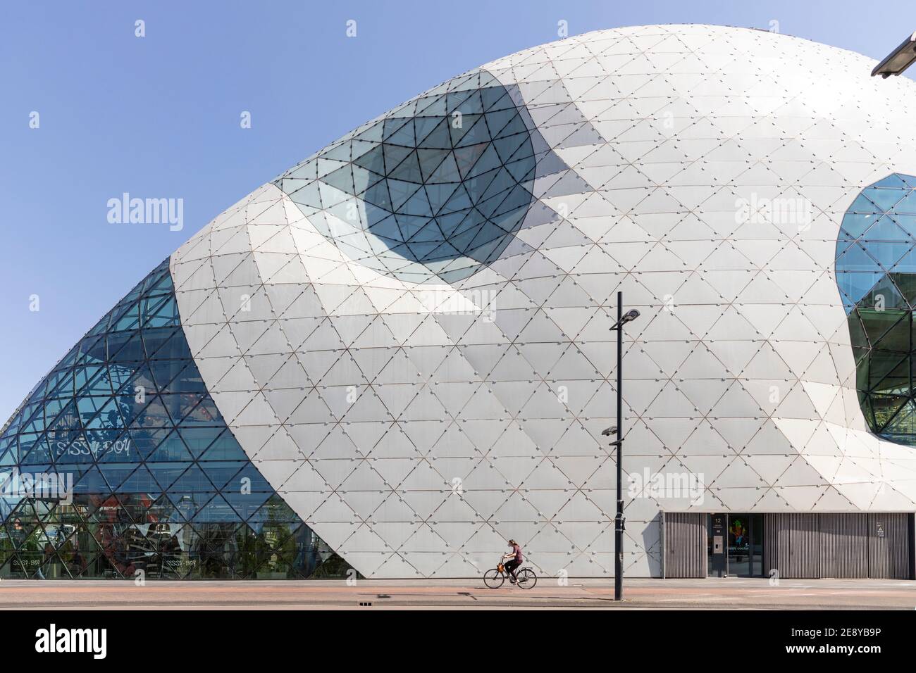 Eindhoven, The Netherlands, April 21st 2020. Exterior of the famous ’Blob’ building designed by Massimiliano Fuksas. A cyclist passing by on a sunny d Stock Photo