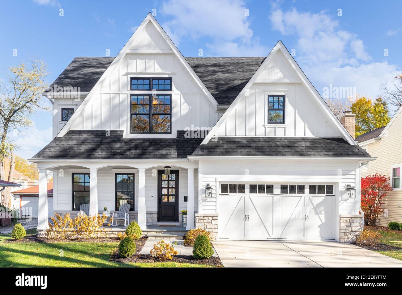 A new, white modern farmhouse with a dark shingled roof and black