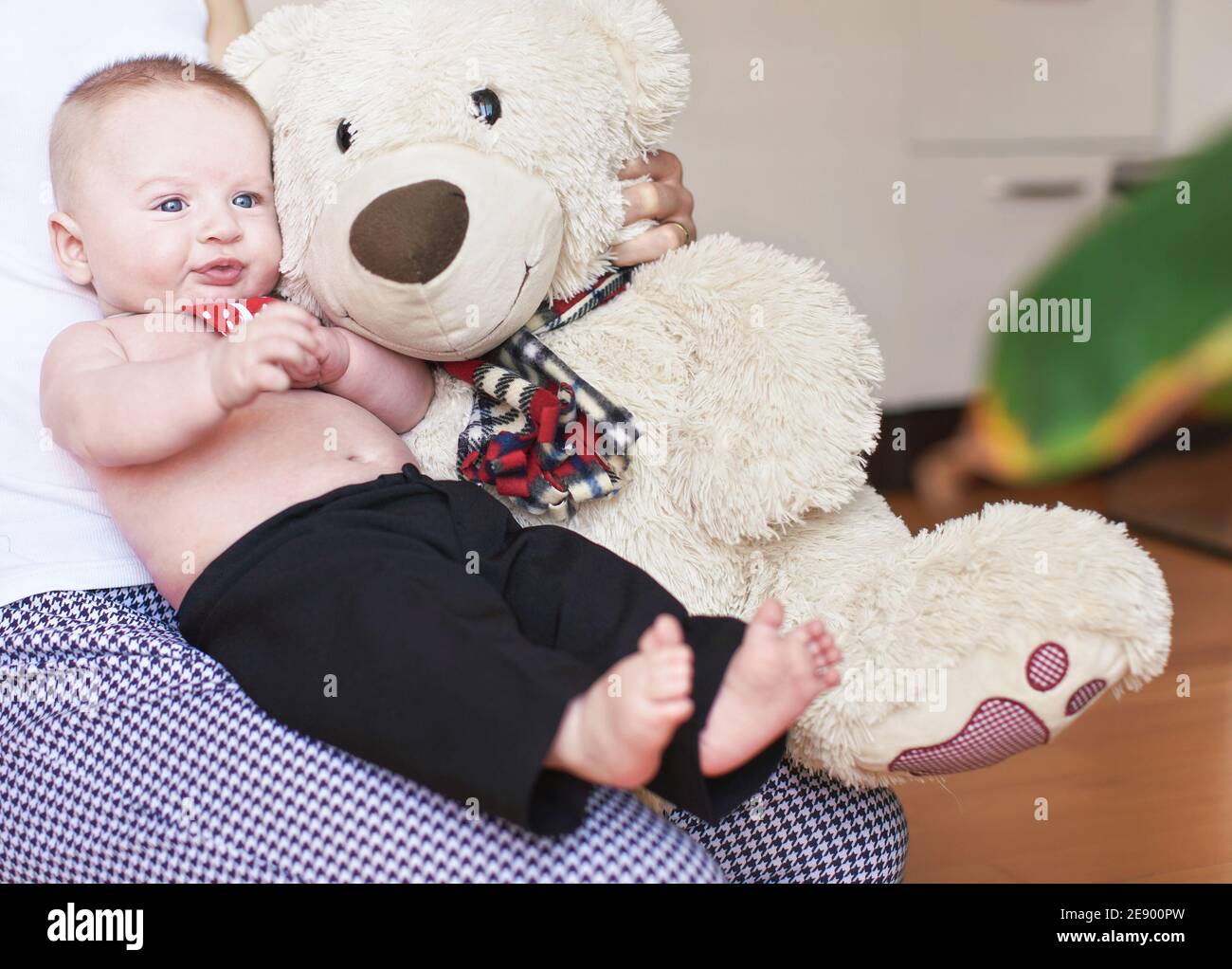 Four months old baby boy sitting on her mother knees, large plush teddy