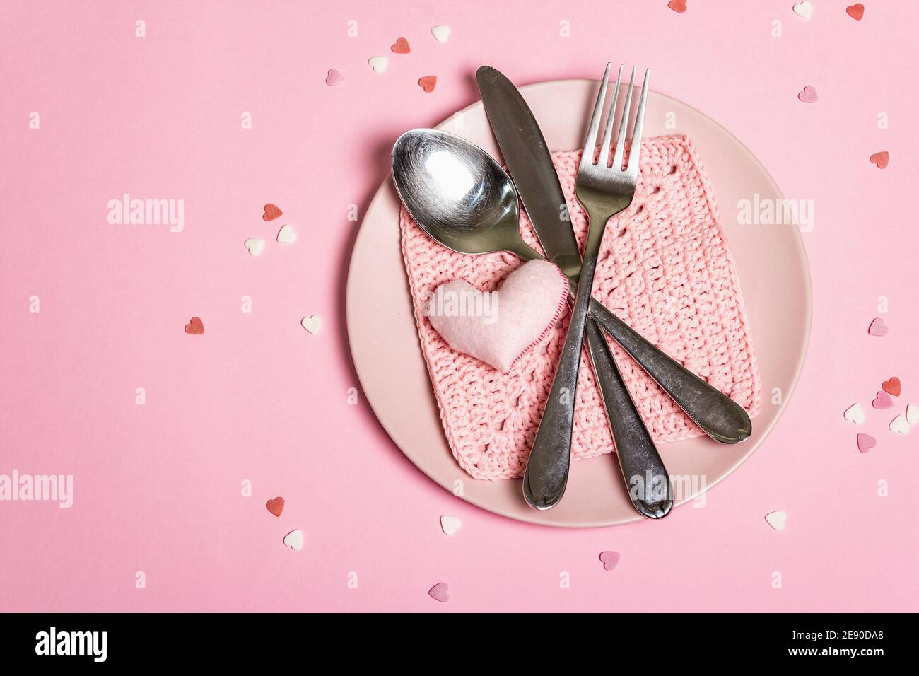 Romantic dinner table. Love concept for Valentine's or mother's day, wedding cutlery. Minimalistic style, rose plates, crochet napkin, scattered pastr Stock Photo