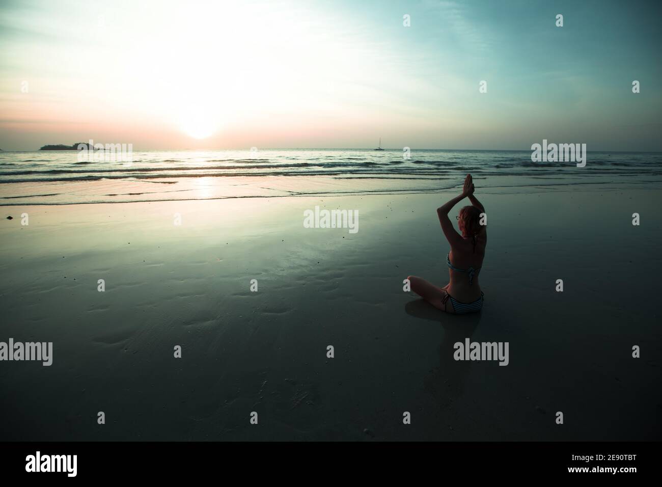 Woman sit at the seaside and meditating in yoga pose during amazing sunset. Stock Photo