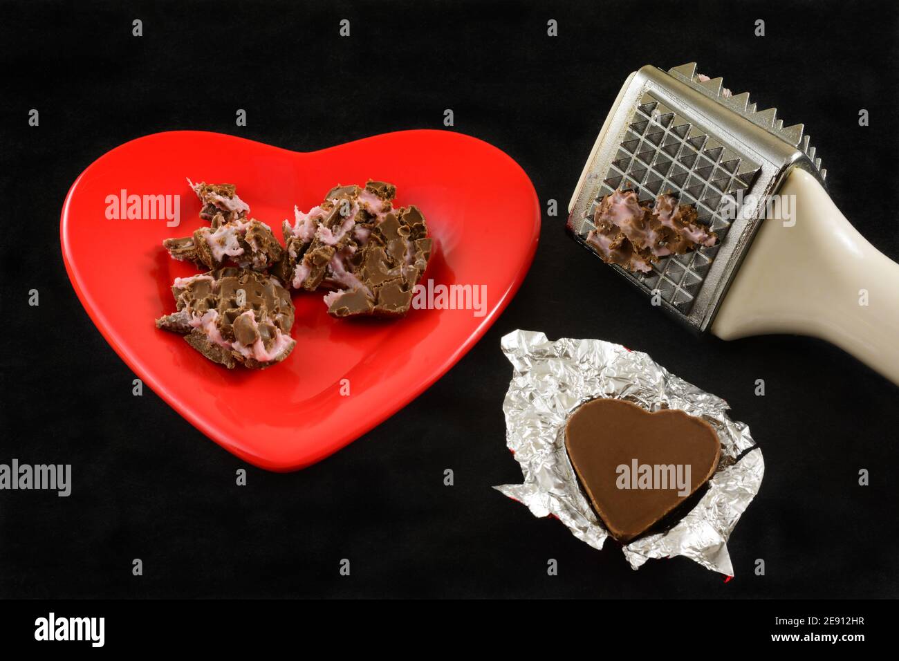Crushed shredded chocolate heart with pink filling and meat tenderizer mallet and chocolate heart in foil as anti-Valentine symbol of divorce or broke Stock Photo