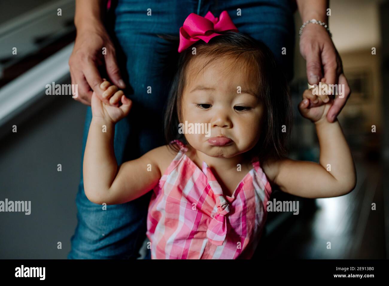 Pouting asian toddler with pink bow in hair learning to walk Stock Photo