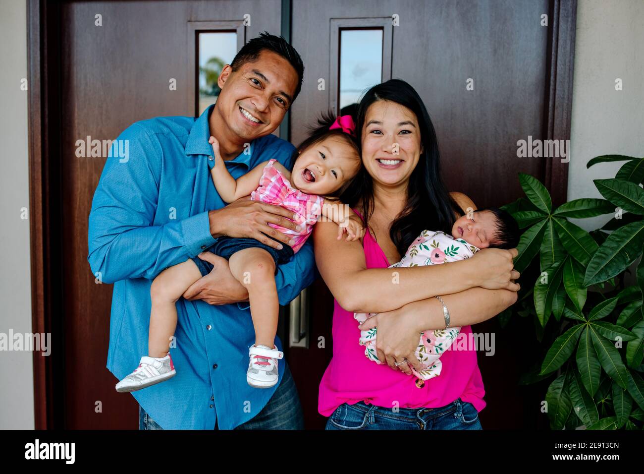 Laughing AsianAmerican family with newborn and yearold daughter Stock