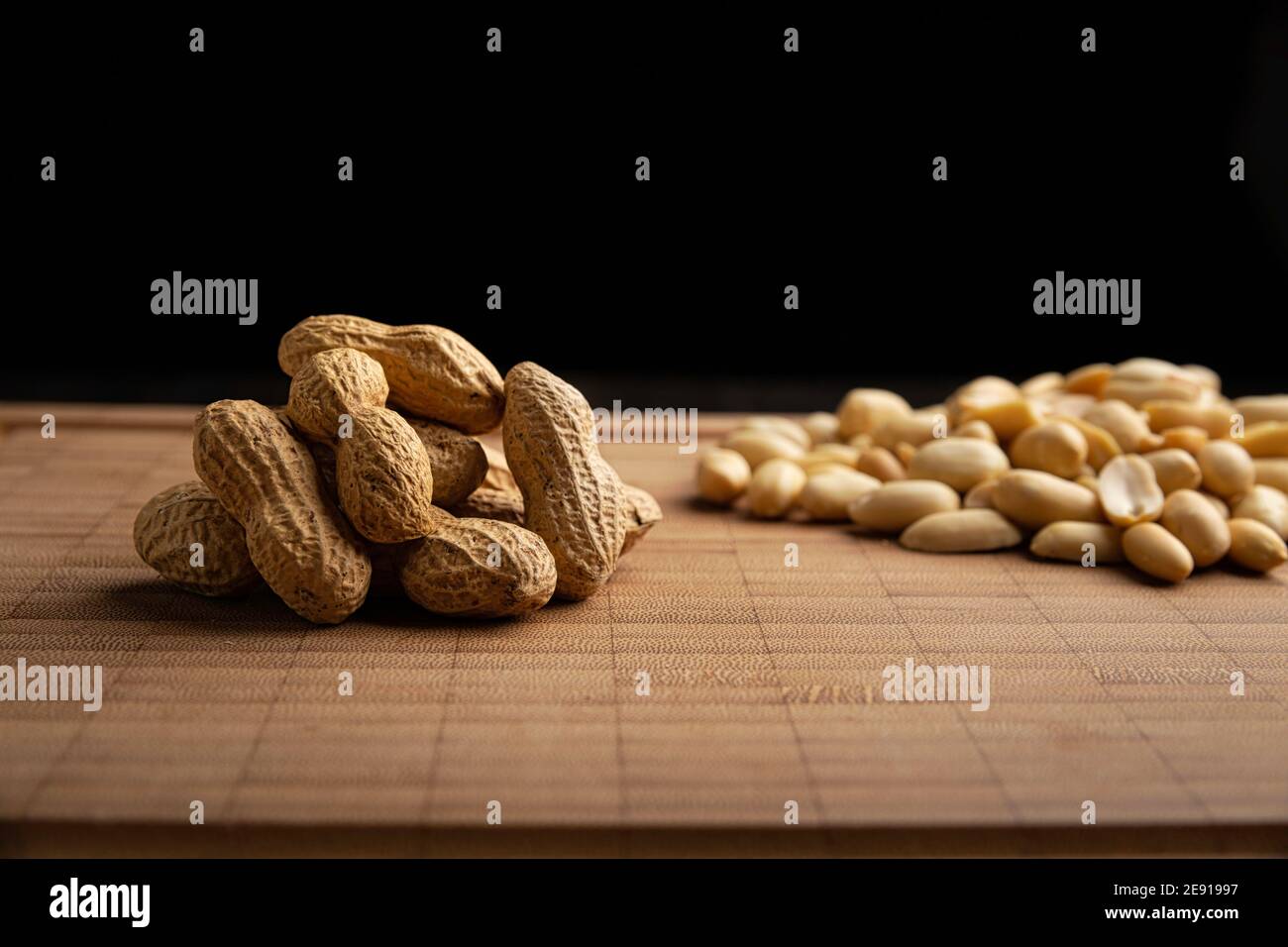 peeled and unpeeled peanuts seeds and on bamboo cutting table with black background. (arachis hypogaea) Edible seeds. Healthy snack nutrition concept Stock Photo
