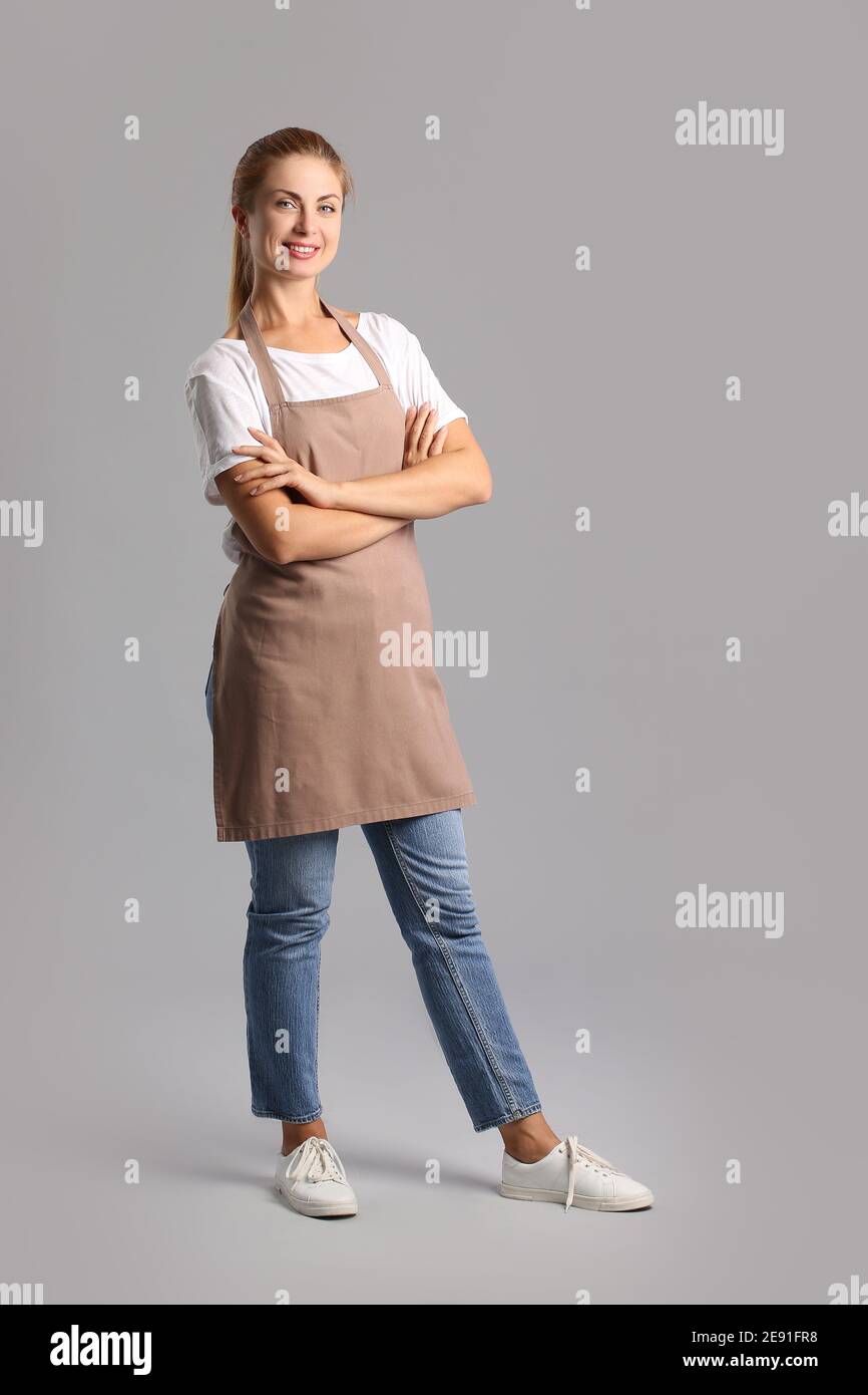 Beautiful young woman wearing apron on grey background Stock Photo - Alamy