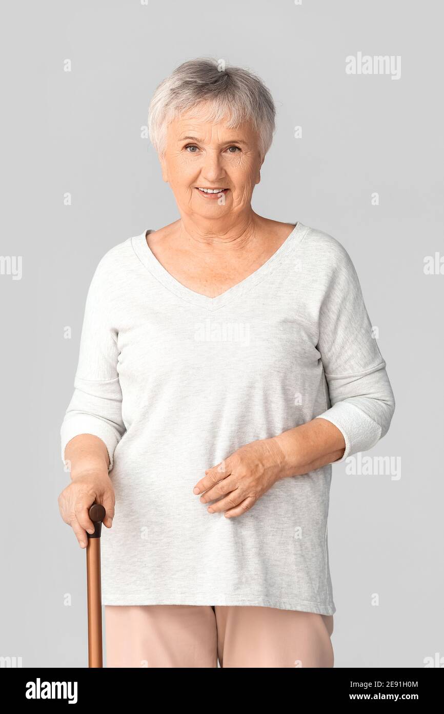 Senior woman with walking stick on light background Stock Photo - Alamy