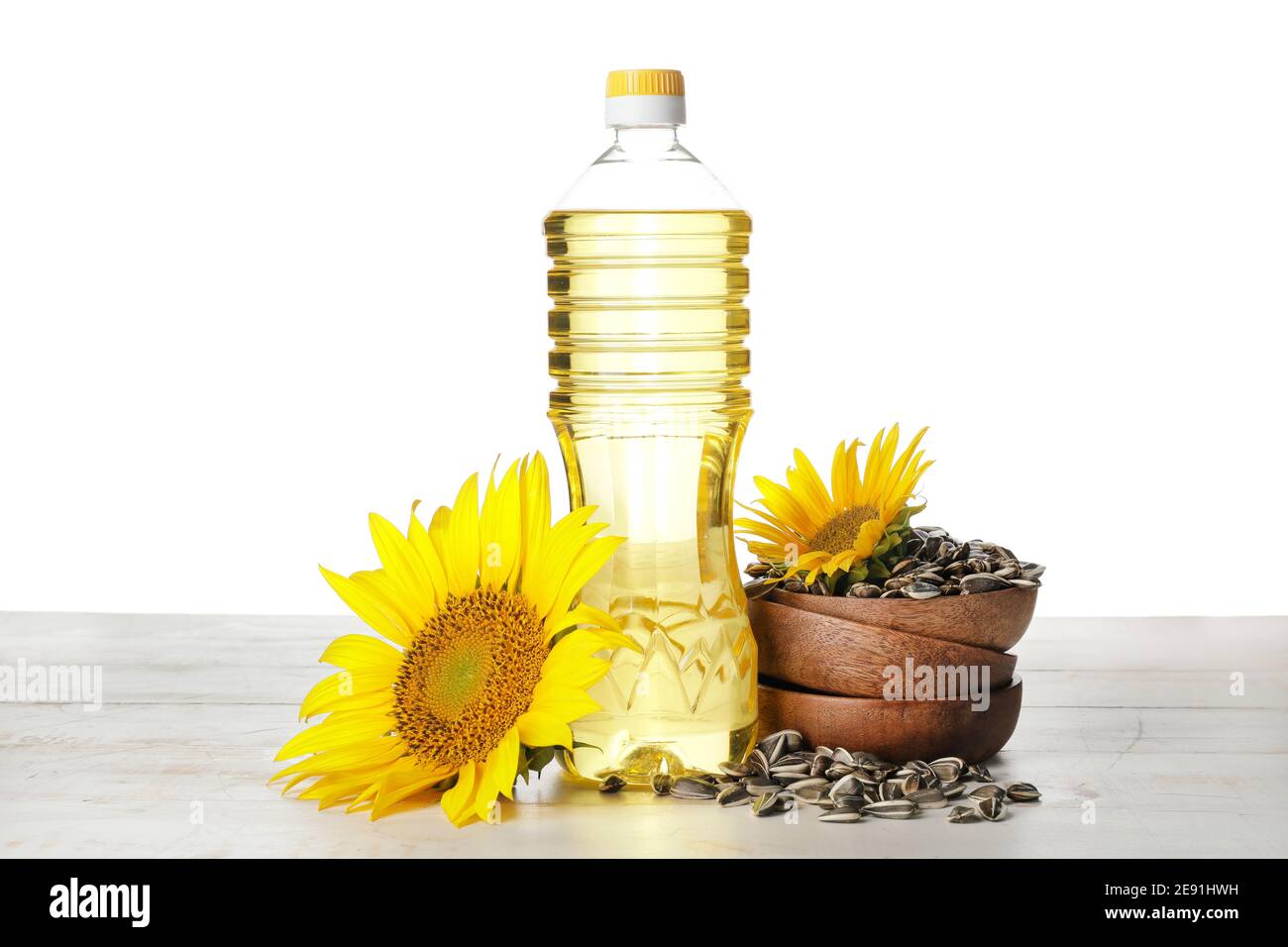 Bottle of oil, bowl with seeds and sunflowers on table against white ...