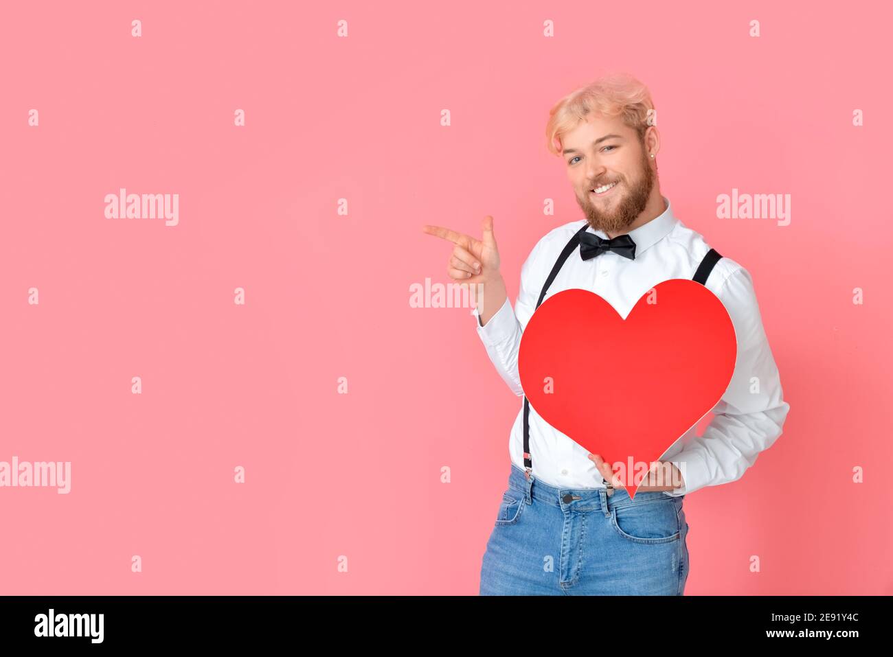 Handsome man with big red heart pointing at something on color ...