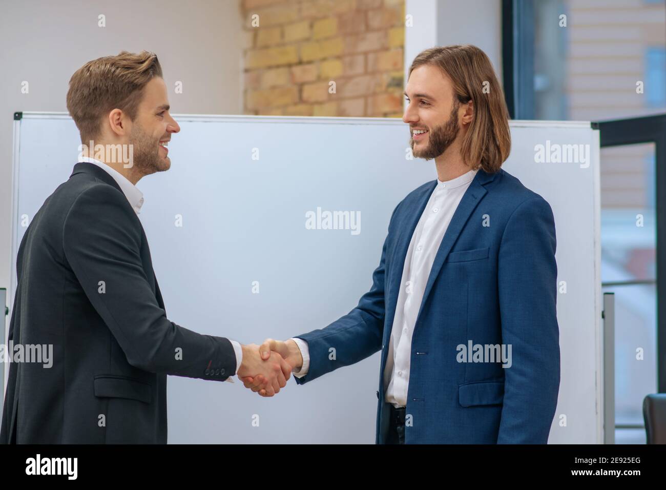 Two smiling men in business suits shaking hands Stock Photo Alamy