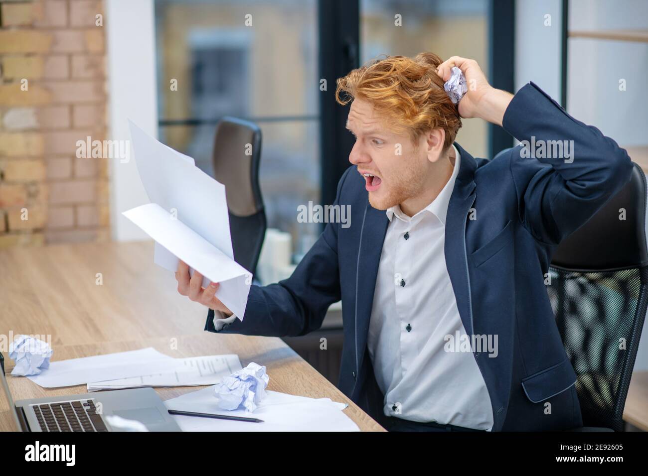 Surprised man holding crumpled documents at workplace Stock Photo