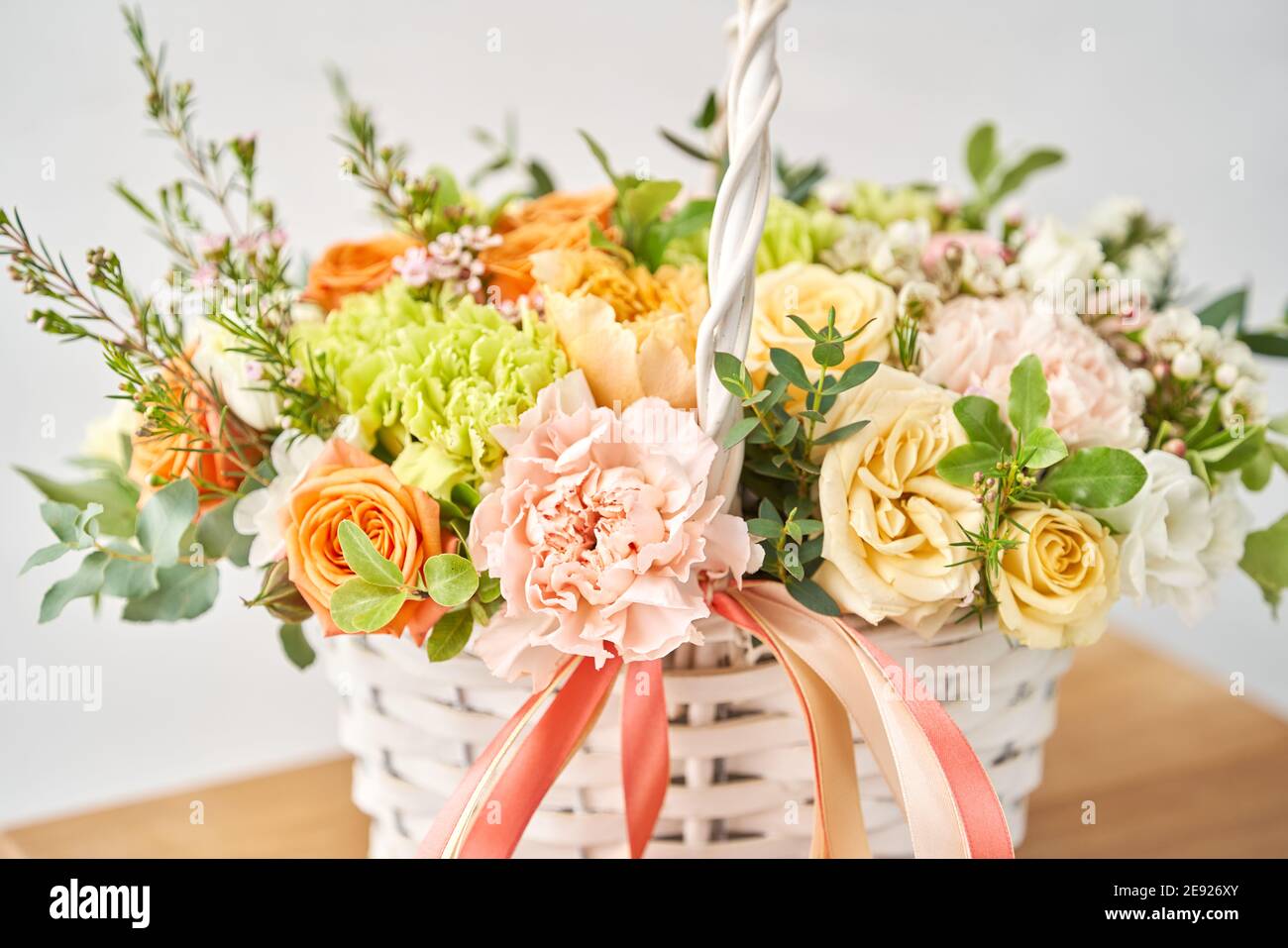 Small flower shop and Flowers delivery. Flower arrangement in Wicker basket. Beautiful bouquet of mixed flowers on wooden table. Handsome fresh Stock Photo
