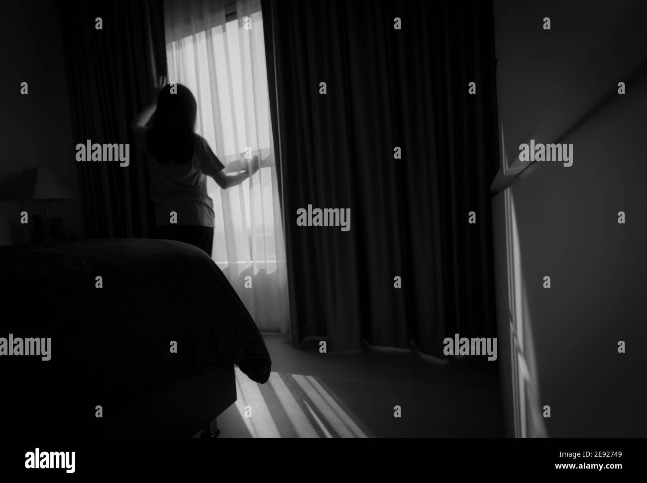 Rear view of woman holding curtain and looking out of glass window. Depressed woman from lock down and quarantine from coronavirus pandemic. Mental. Stock Photo