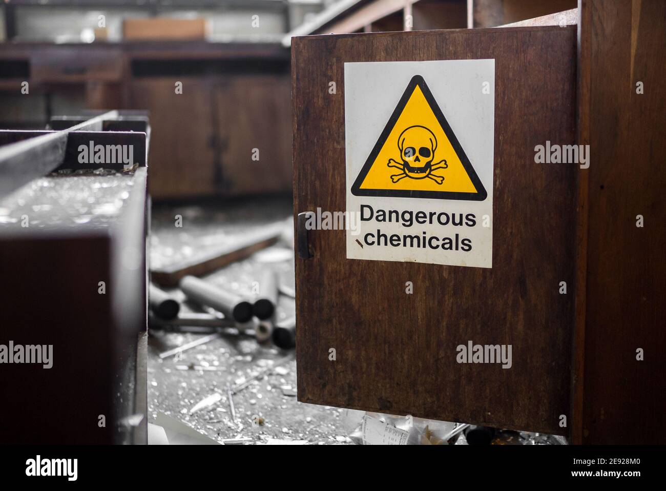 Yellow triangle with black skull and crossbones dangerous chemicals sign on open wooden cupboard door in abandoned laboratory after burglary equipment Stock Photo