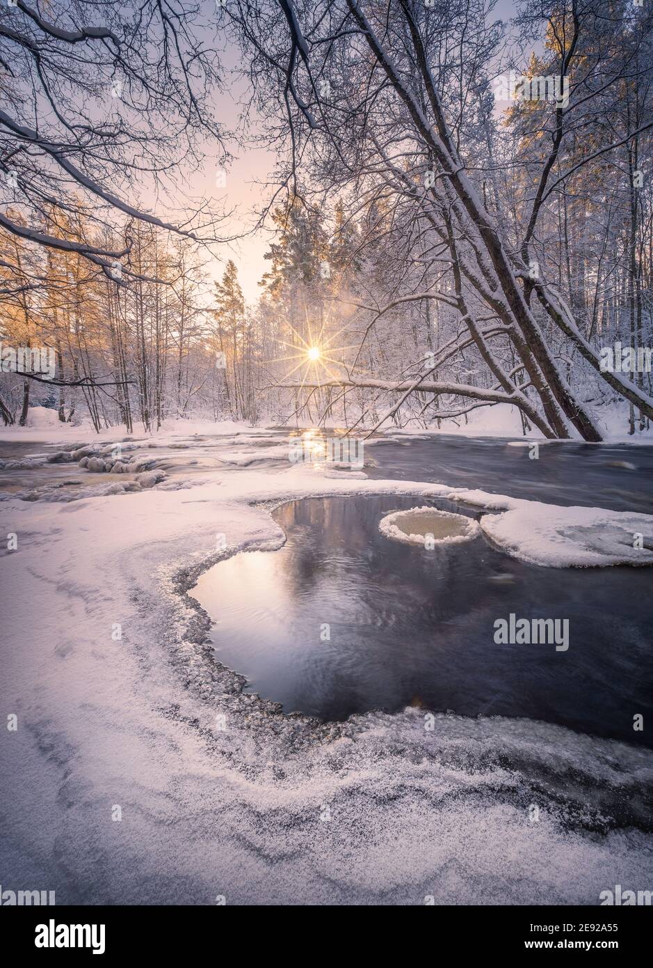 Scenic winter landscape with flowing river and morning light in Finland. Snowy trees. Stock Photo