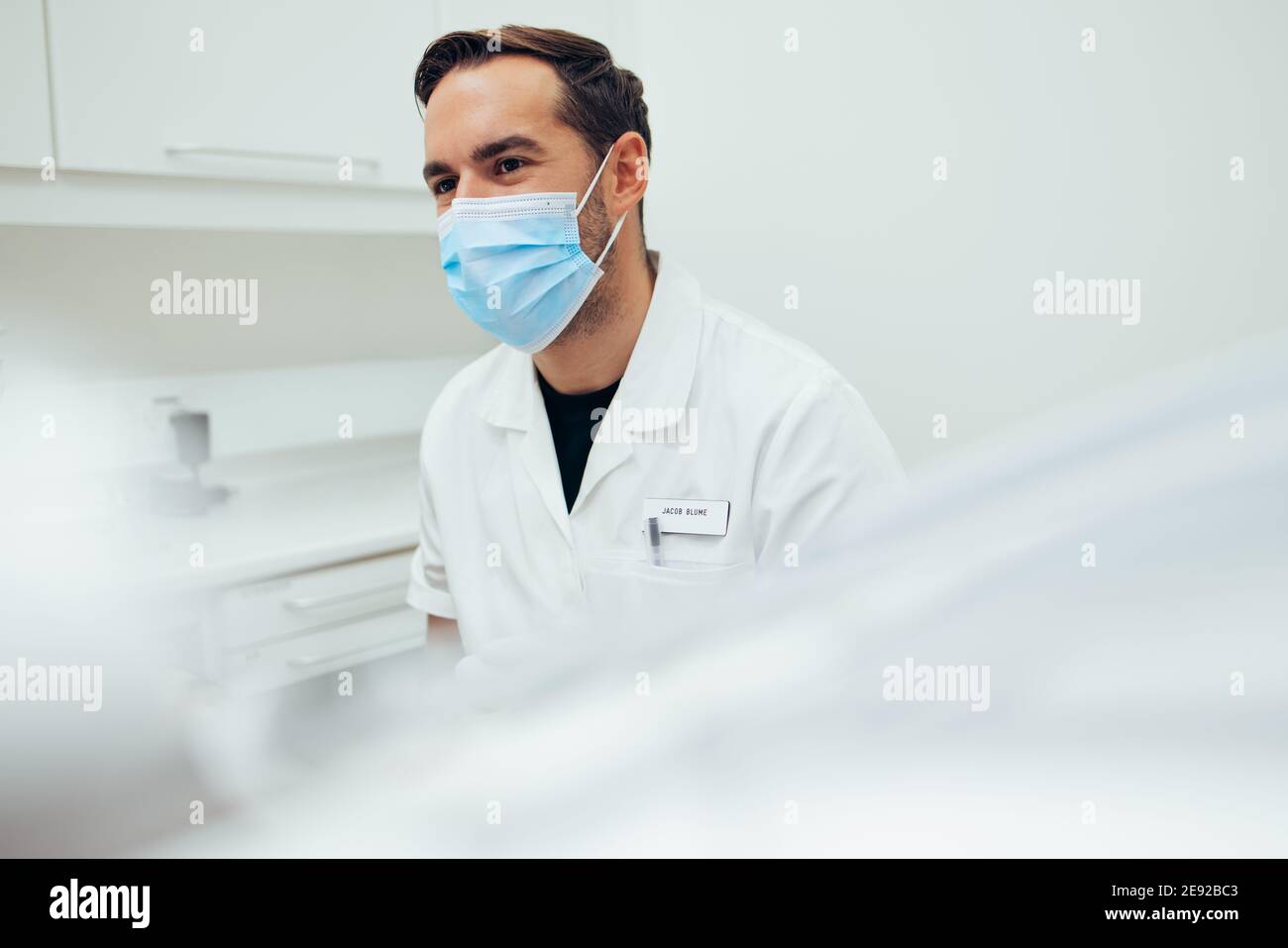 Male dental doctor wearing face sitting at his clinic. Dentist with a face mask at dentistry. Stock Photo