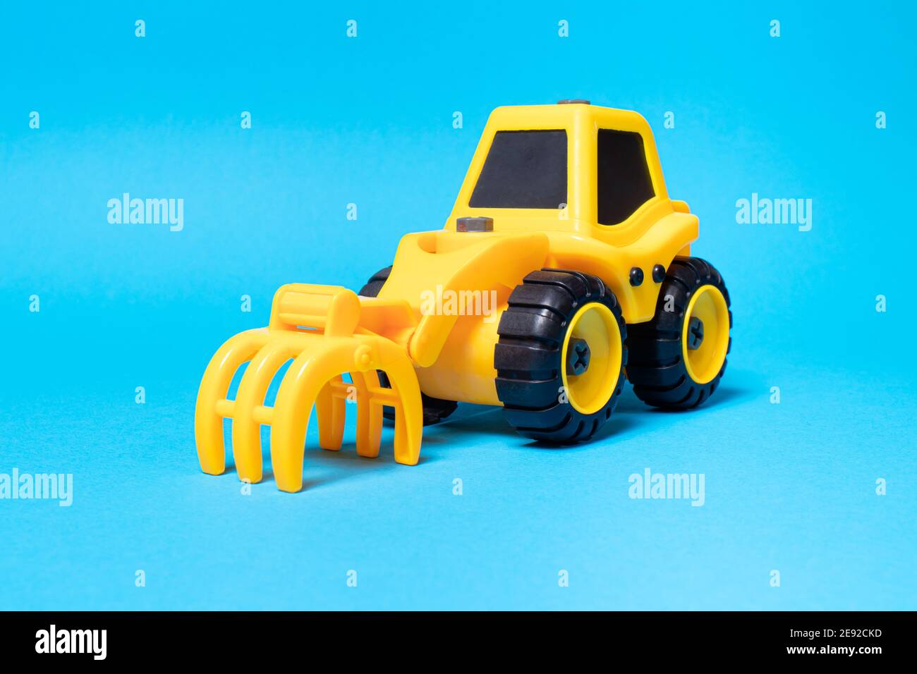 Yellow toy tractor with rake nozzle to load the forest on a blue ...