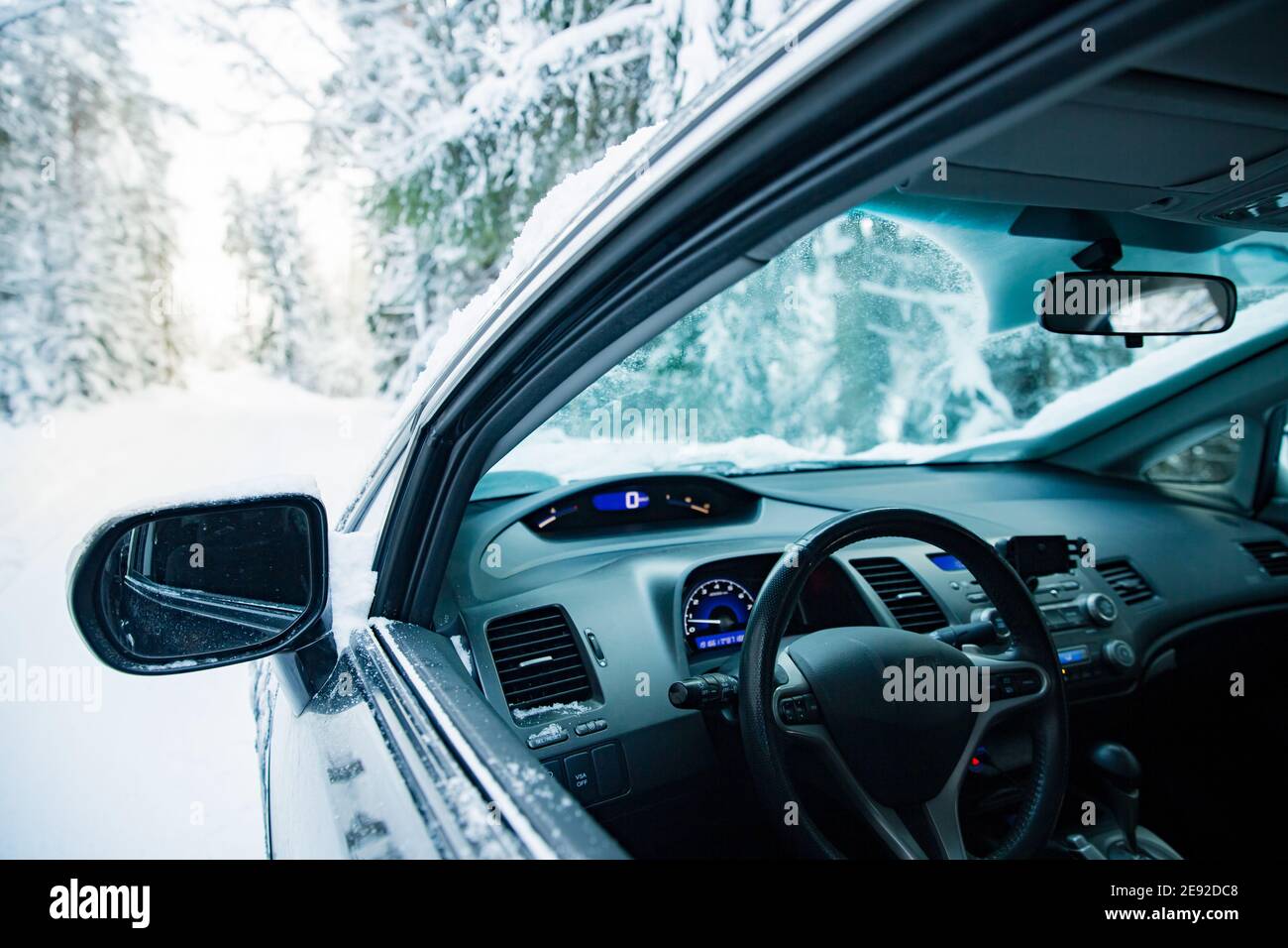 Car covered with snow and ice driving on the winter road. Beautiful landscape of winter forest and snowy country side. Stock Photo