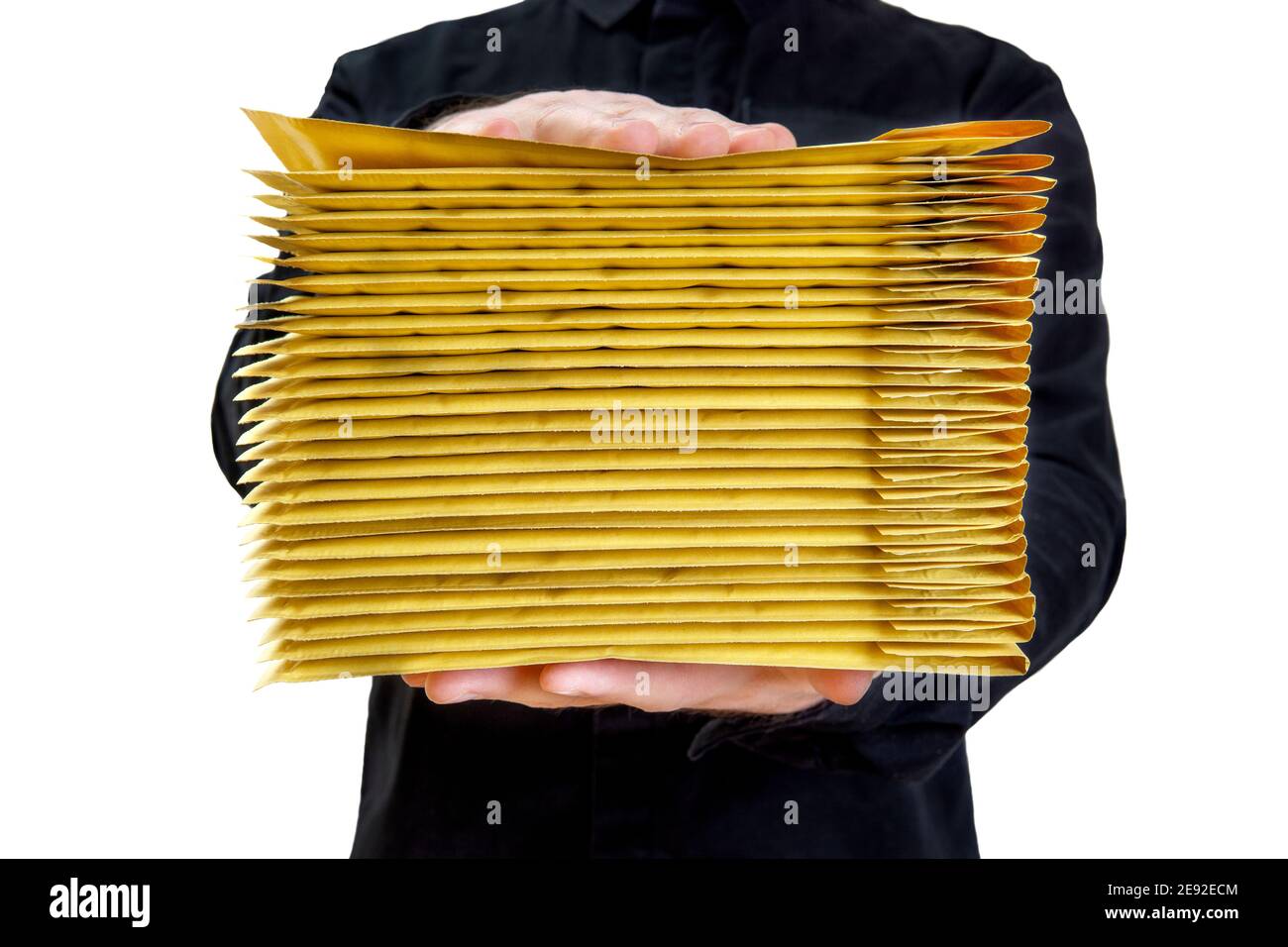 Man wearing a black uniform holding a stack of yellow padded bubble envelopes isolated on white. Stock Photo