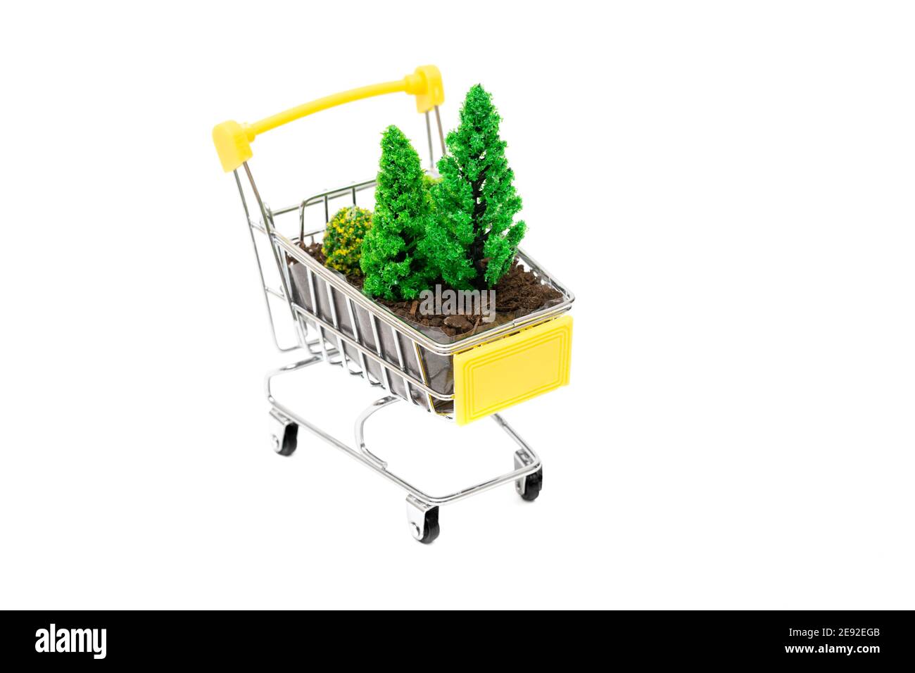 Close-up of a small shopping trolley with soil and toy trees isolated on white. Creative forests care concept. Stock Photo