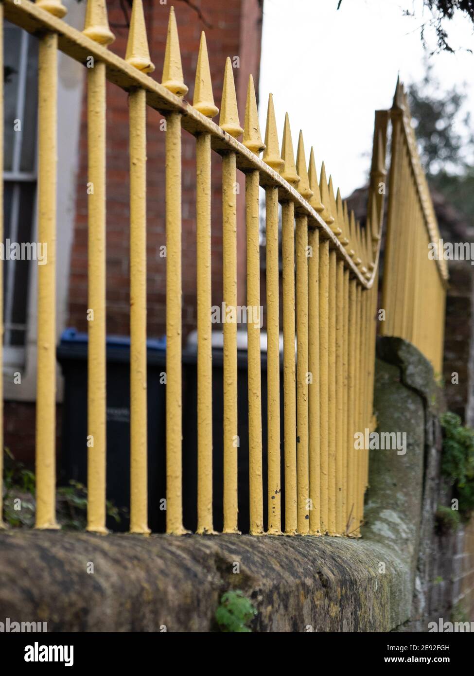 Wrought iron, pointed railings painted yellow on a stone wall in ...