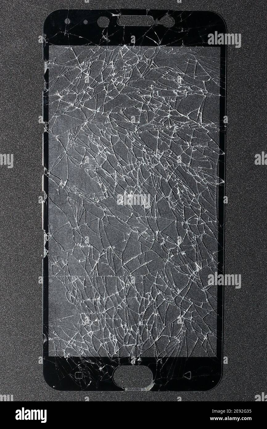 The phone's screen protection film is completely broken and rests on a black-gray background. Stock Photo