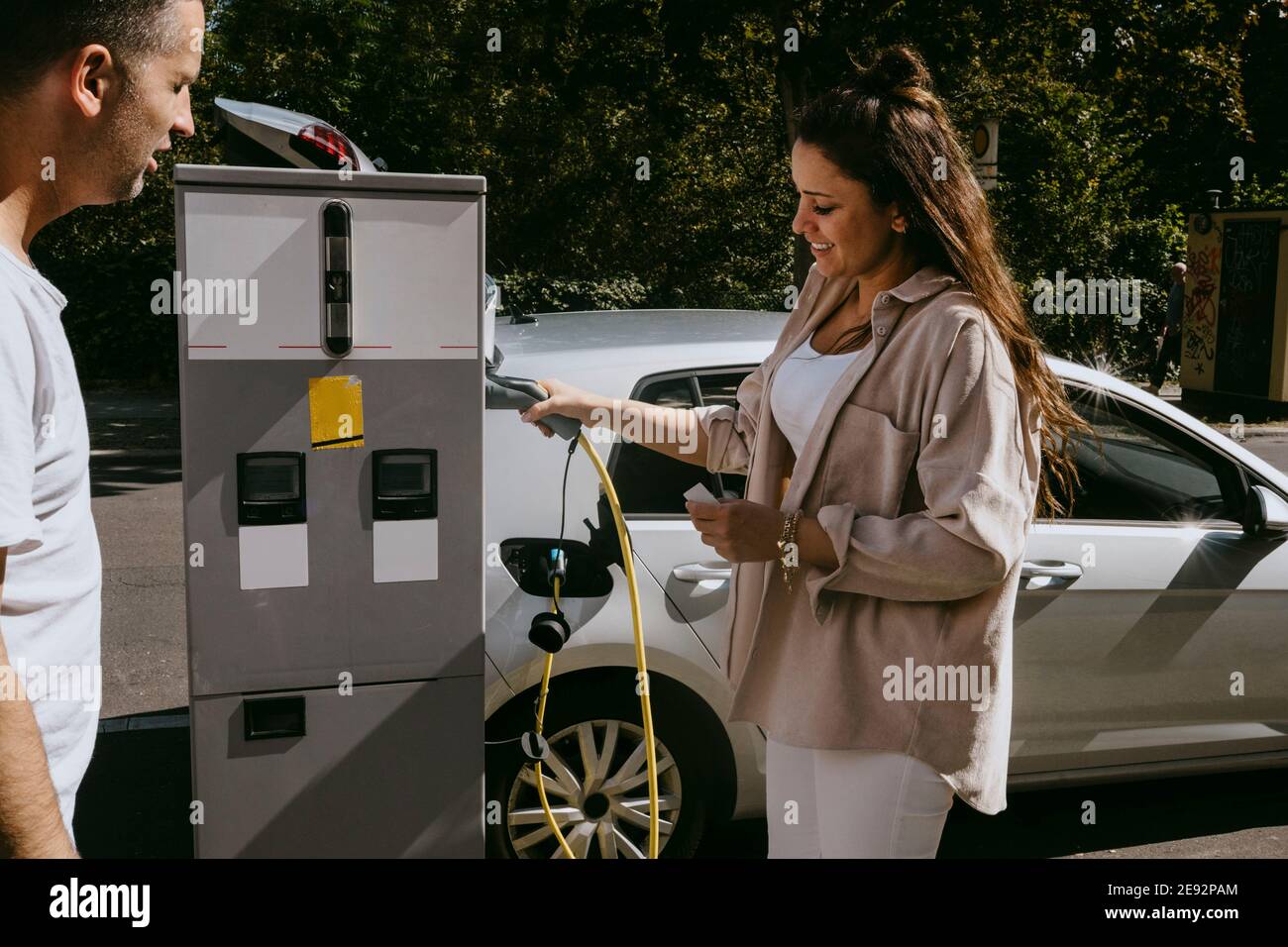Smiling mother holding electric plug standing by father at gas station Stock Photo