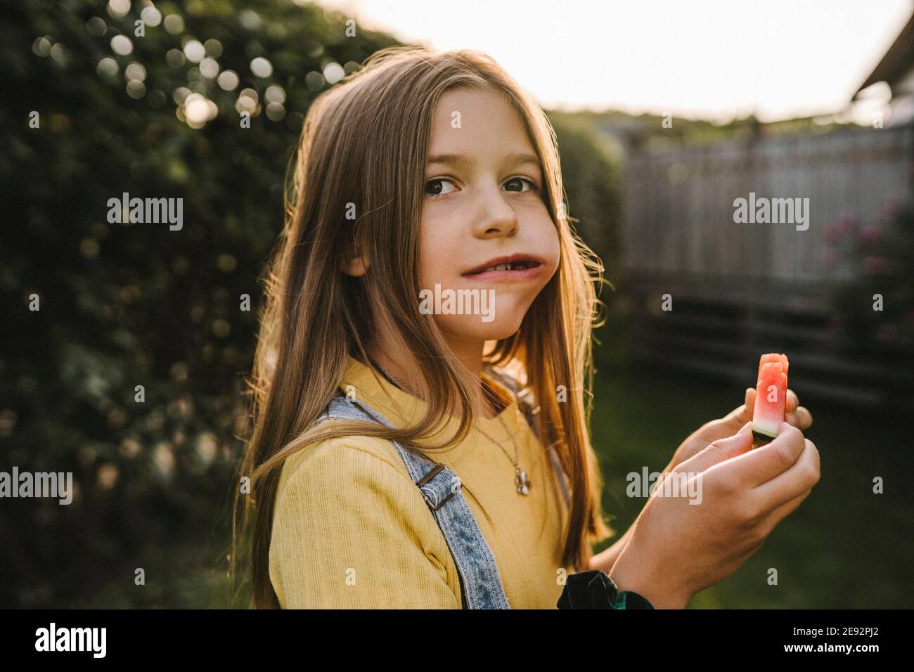 Pre-adolescent girl looking away while eating watermelon in back yard Stock Photo