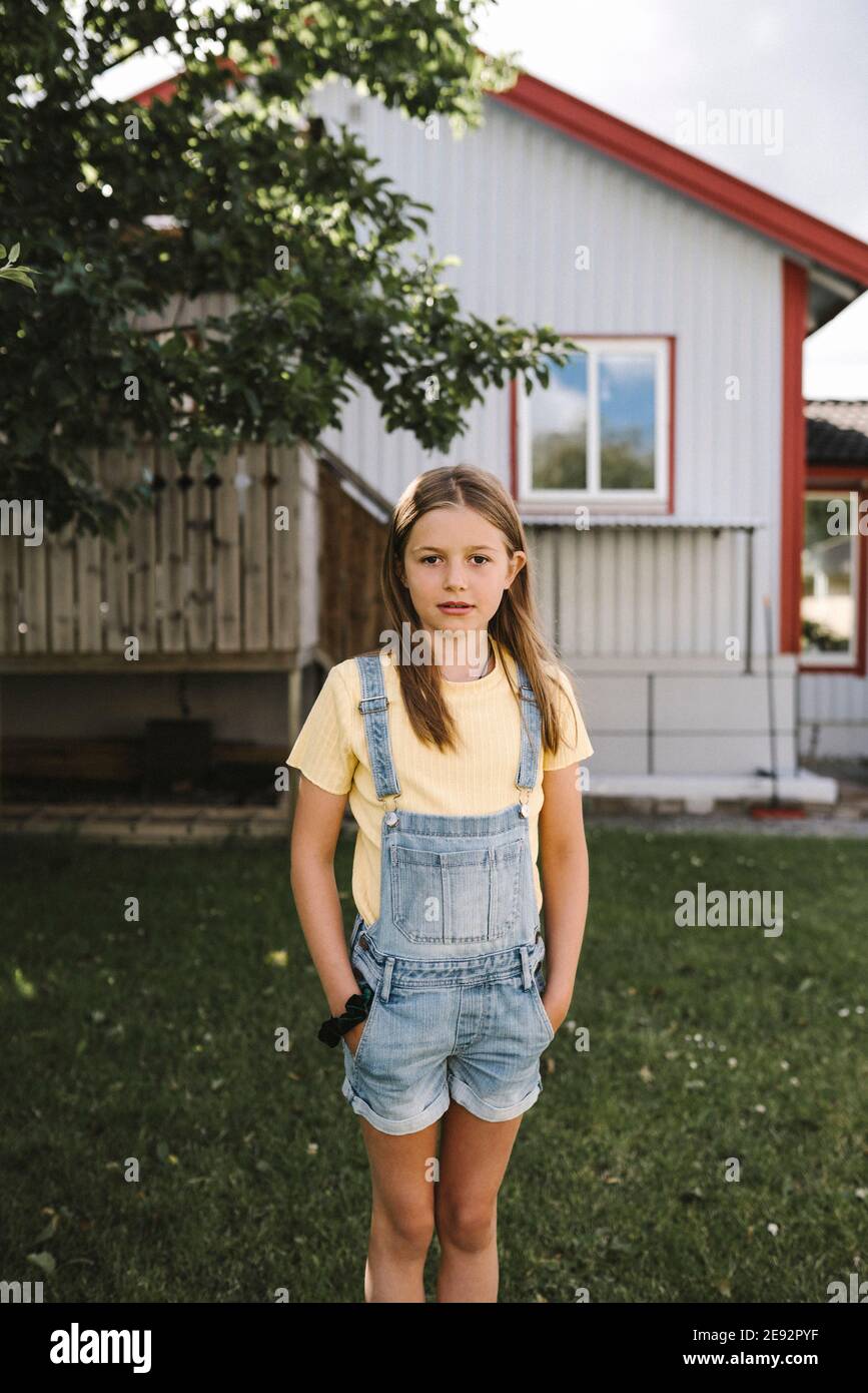 Pre-adolescent girl with hands in pockets standing in back yard Stock Photo
