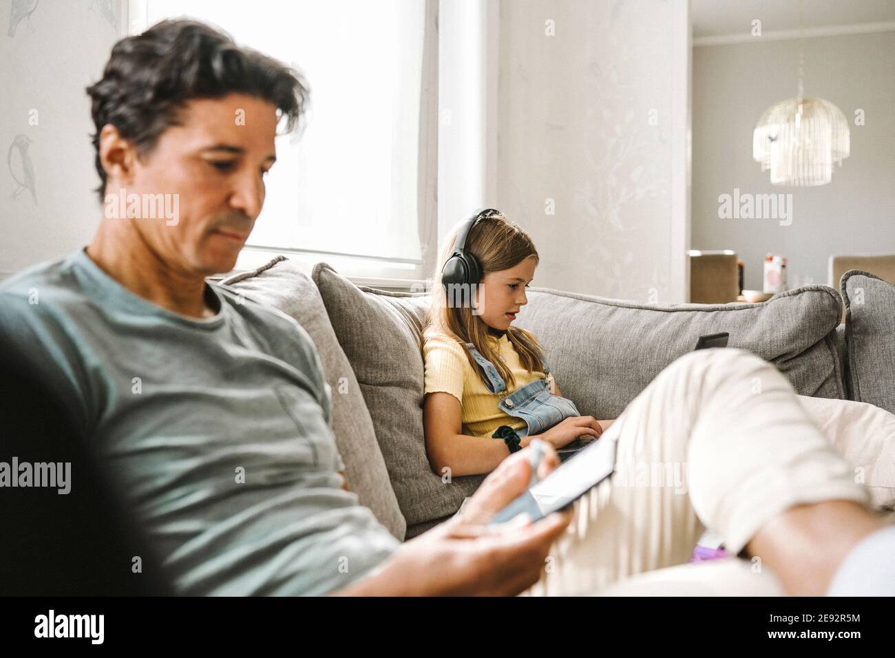 Father using smart phone while daughter e-learning through laptop in living room Stock Photo