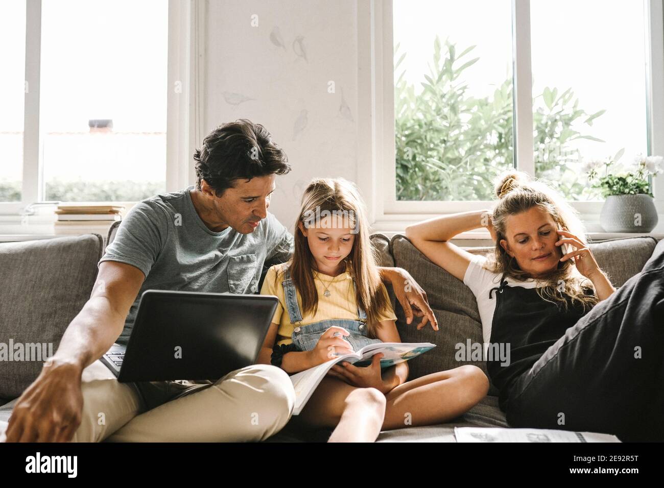 Daughter doing homework sitting by mother and father in living room Stock Photo