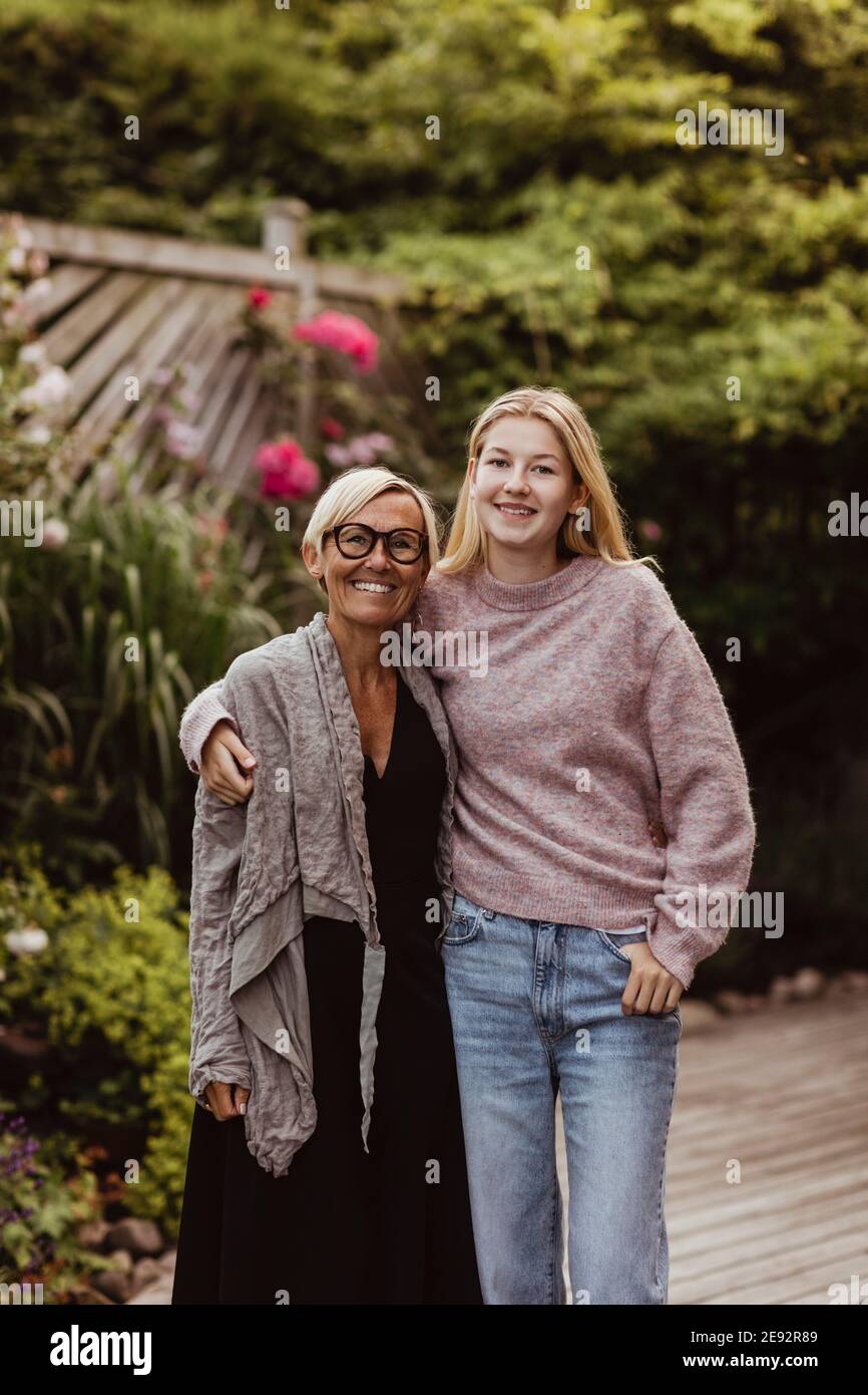 Smiling granddaughter with arm around of grandmother in back yard Stock Photo