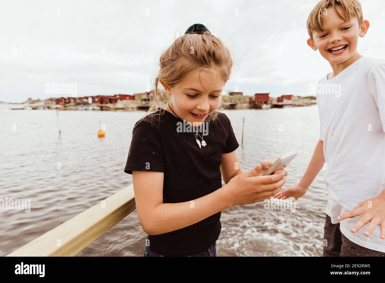 Sister with smart phone standing by smiling brother against sea Stock Photo