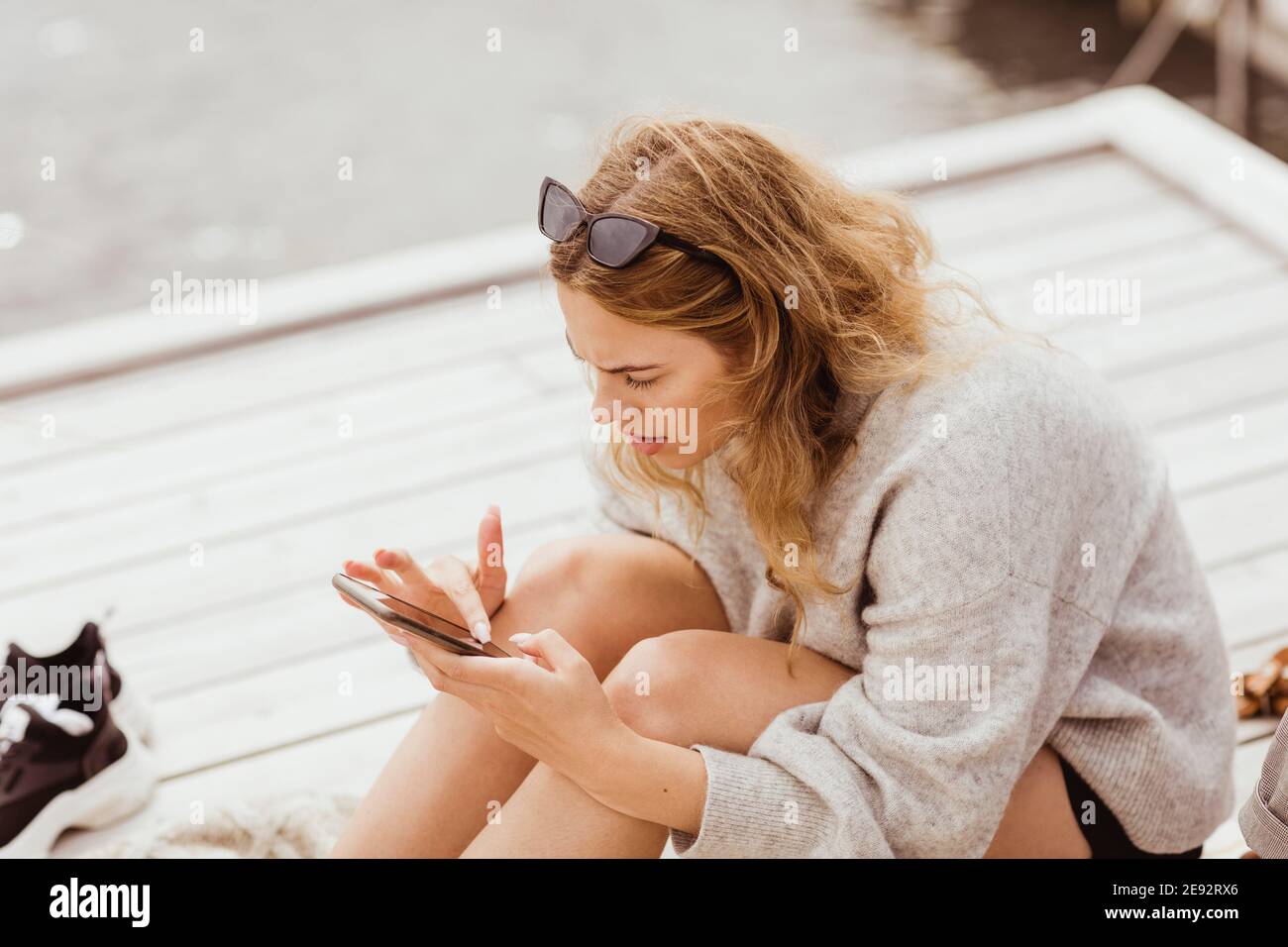 Blond woman using smart phone while sitting on jetty Stock Photo