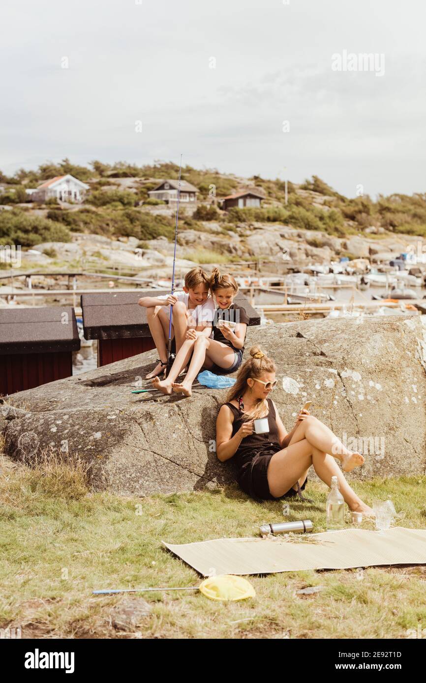 Siblings and mother using mobile phone while sitting at marina Stock Photo