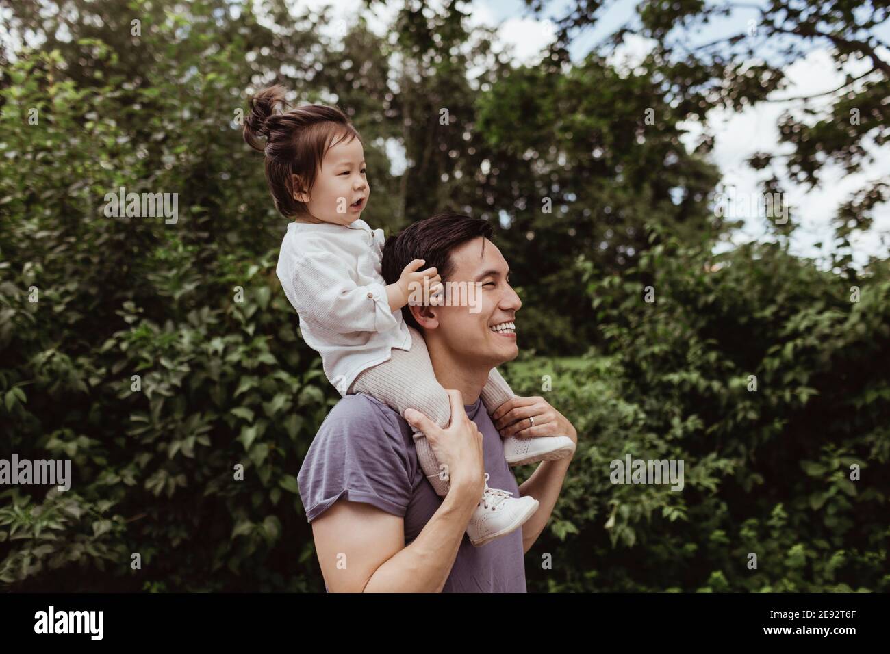 Happy father carrying baby son on shoulder by trees in park Stock Photo