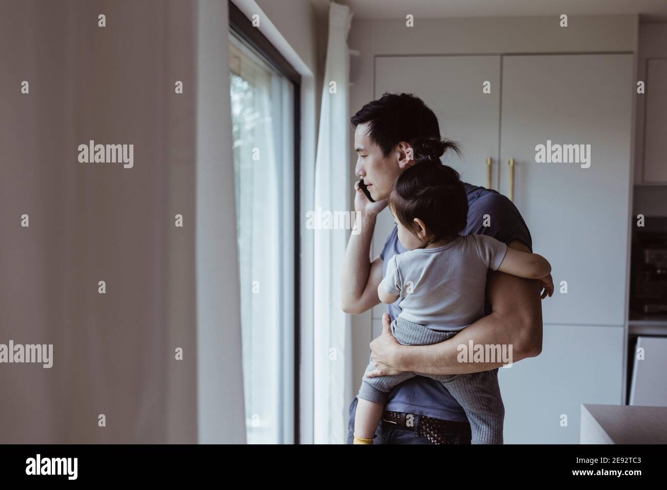 Father talking on mobile phone while carrying son at home Stock Photo