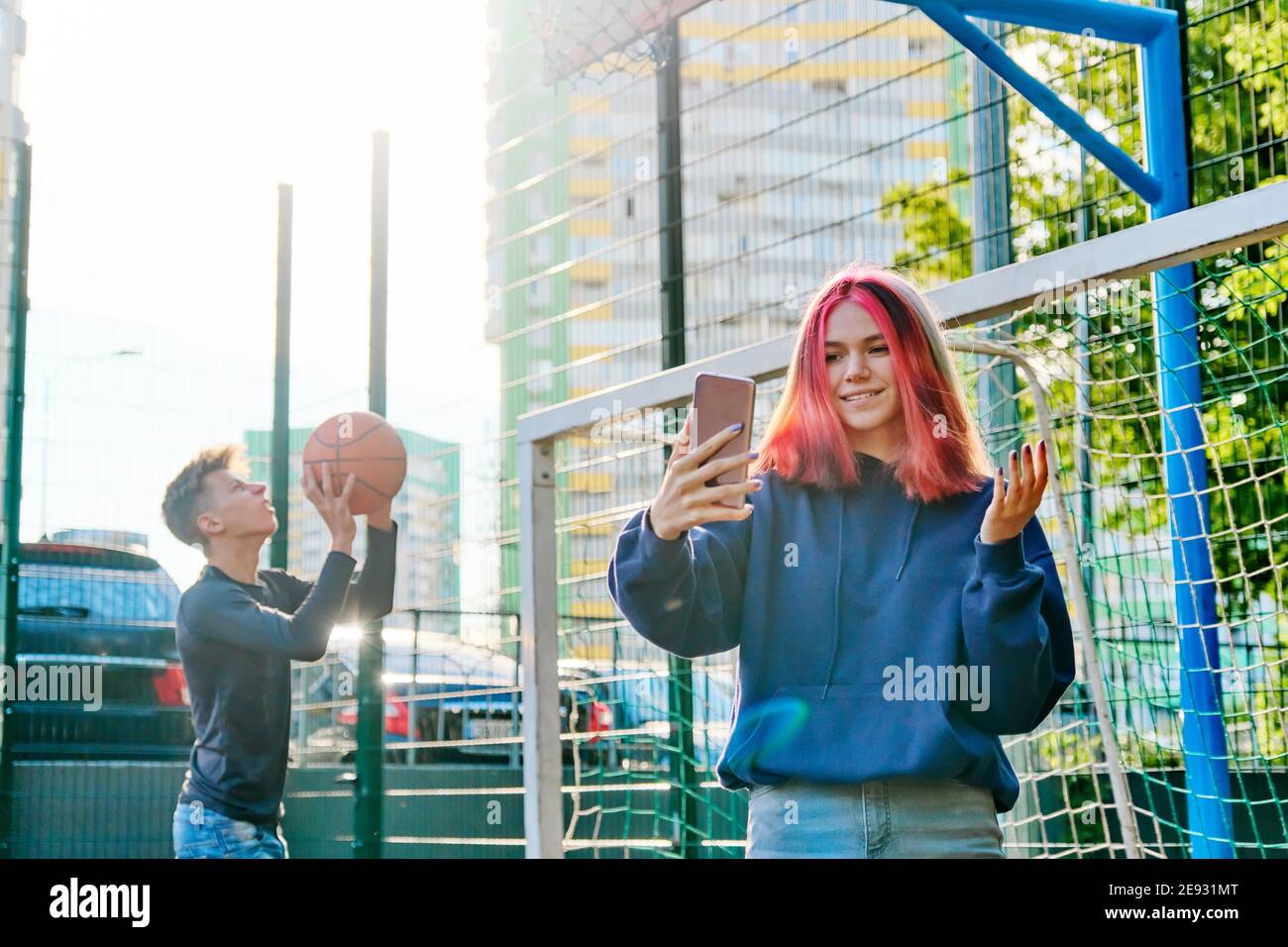Girl teenager recording video stream using smartphone, on sports street  court, guy playing basketball Stock Photo - Alamy
