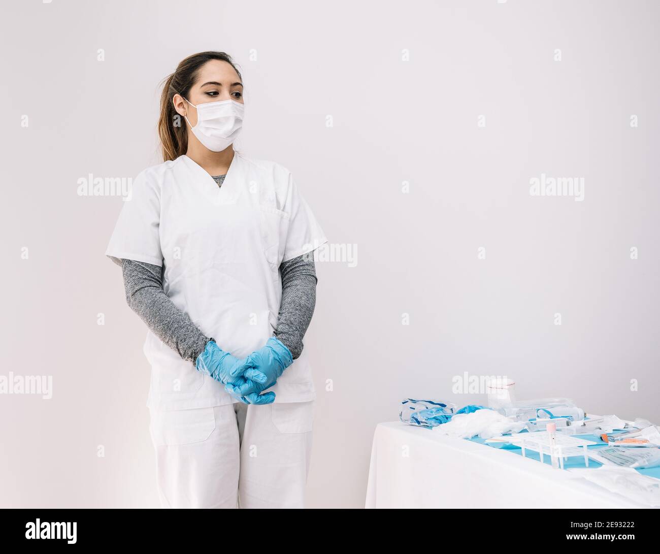 Serious female medic in protective mask and gloves standing near table with assorted equipment for coronavirus diagnostic Stock Photo