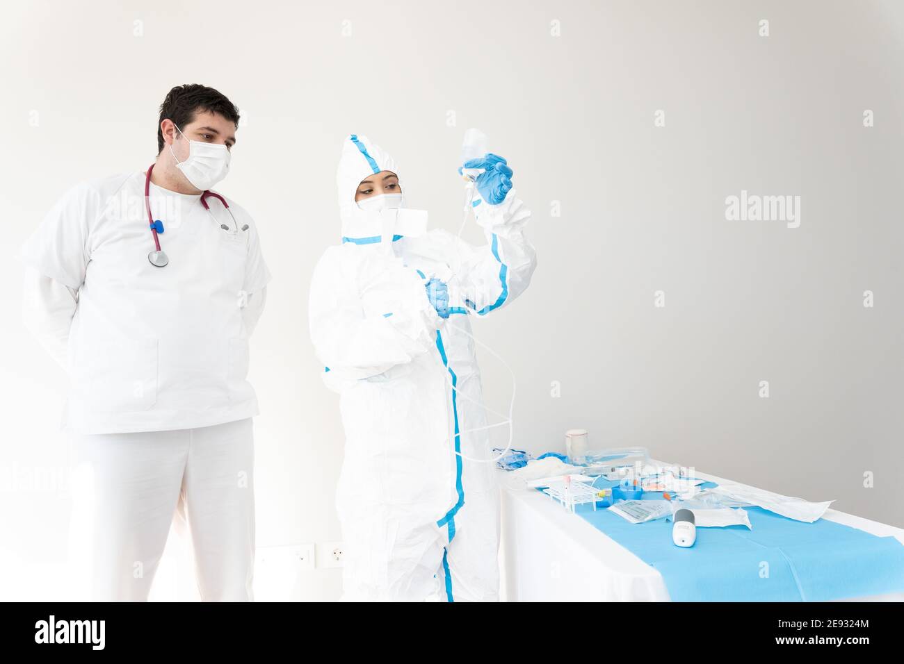 Medic in protective mask and uniform standing with colleague in medical room and using dropper while working in clinic during COVID 19 pandemic Stock Photo