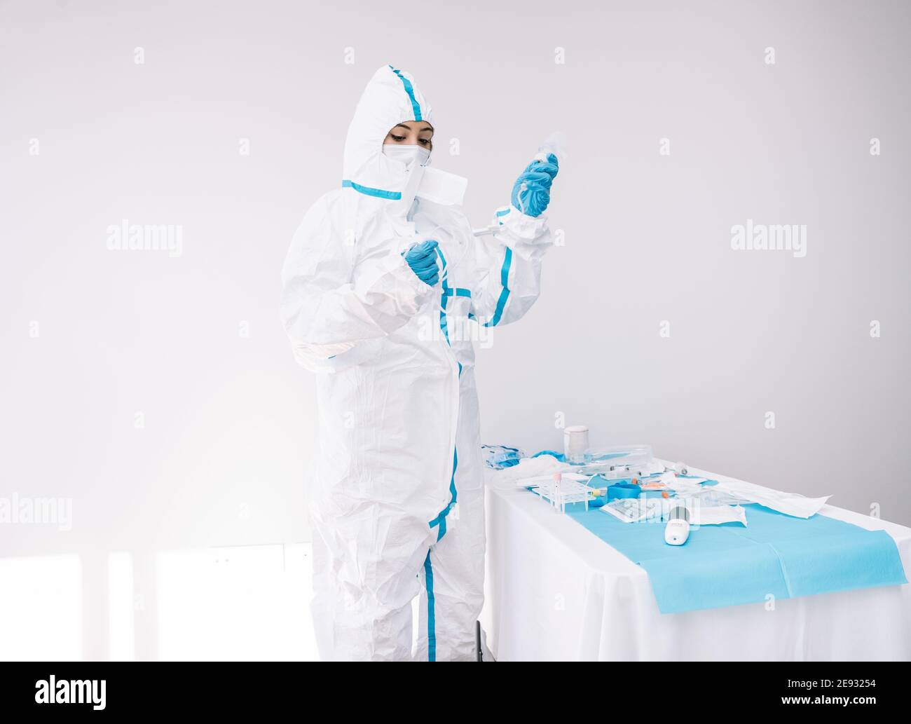 Doctor in medical mask and protective costume standing in hospital and using dropper while working during COVID outbreak Stock Photo