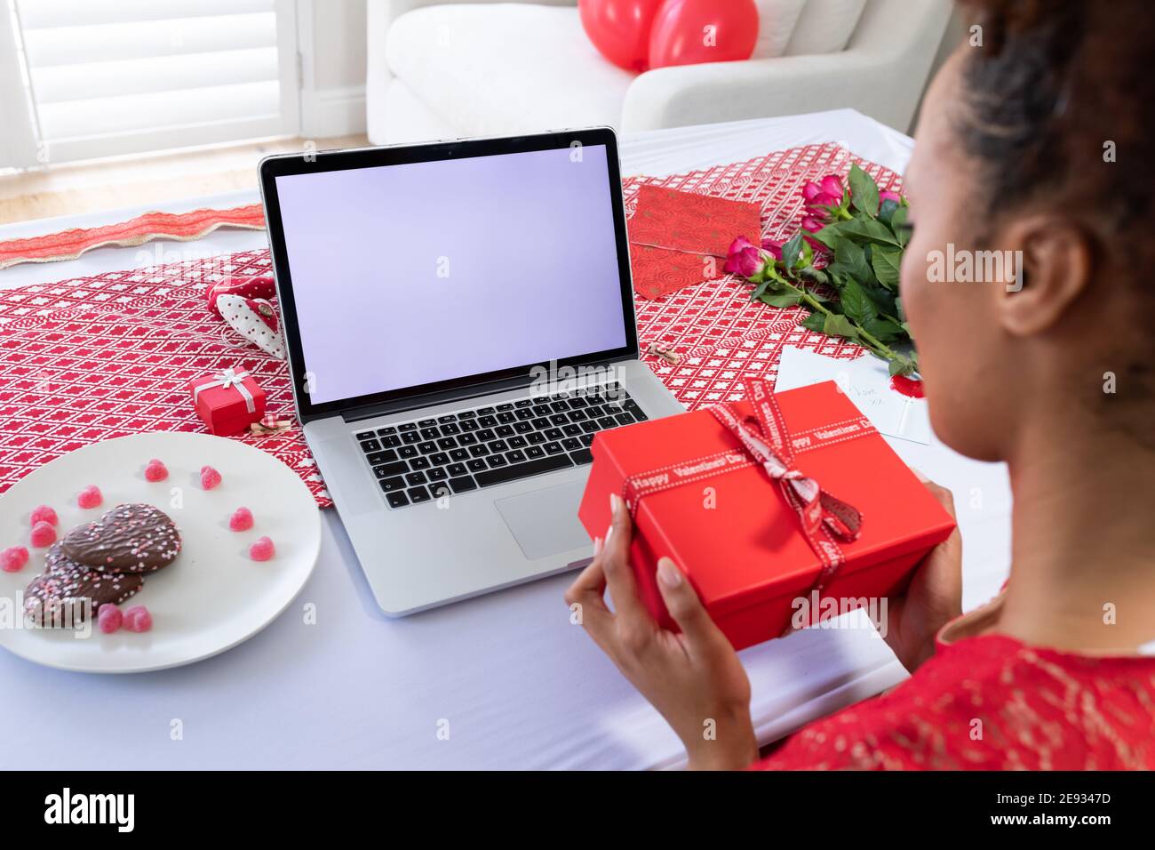 African american woman holding gift box on videocall on laptop at home Stock Photo
