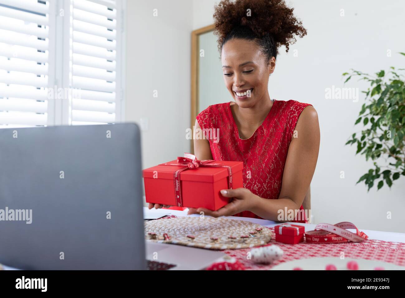 African american woman holding gift box on videocall on laptop at home Stock Photo