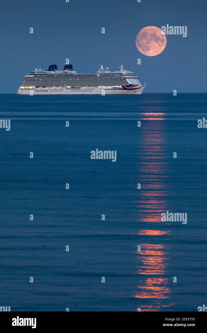 The Harvest Moon rises above P&O Cruises' largest ship, Britannia as she sits at anchor in Weymouth Bay. The cruise industry has suffered a complete s Stock Photo