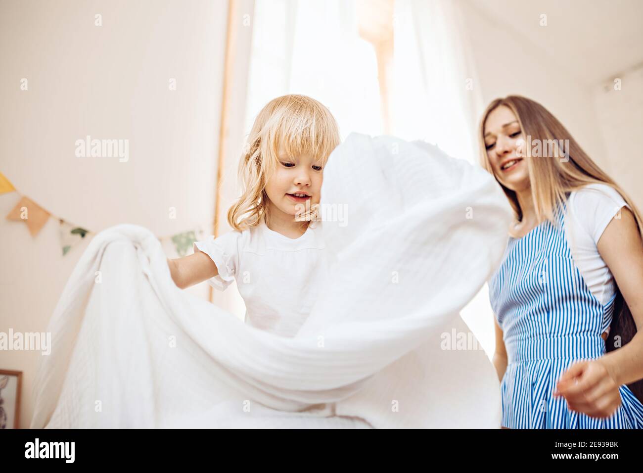 A little girl helps her mother to make the bed. They play and have fun at home Stock Photo