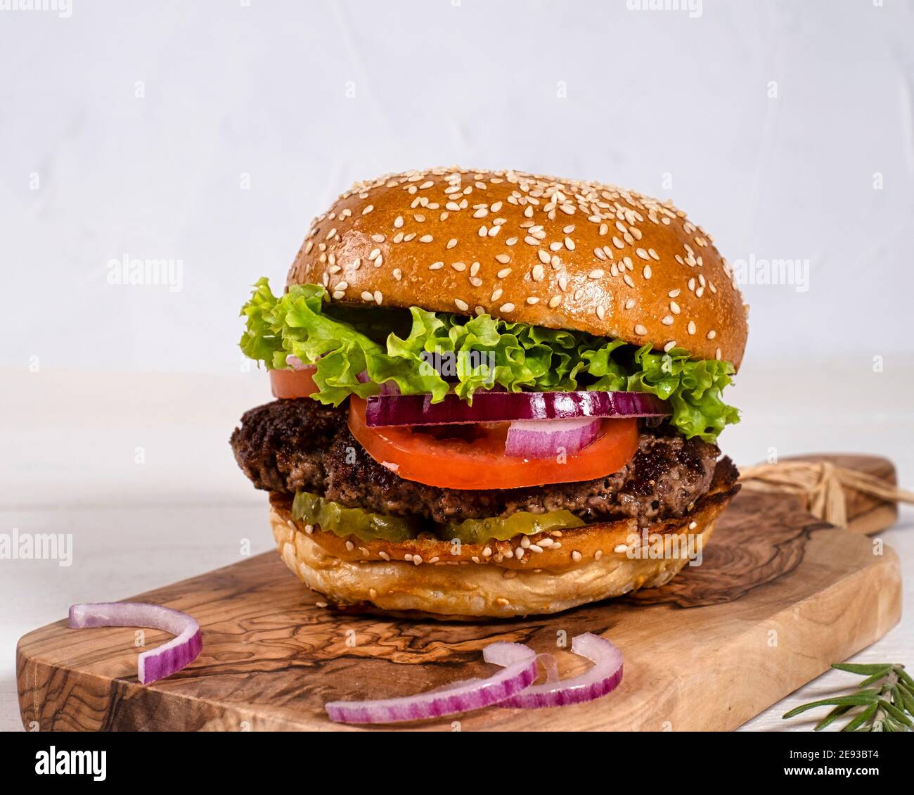 Juicy burger with beef, tomatoes, cucumbers and onions nicely arranged on a wooden board on a white background Stock Photo