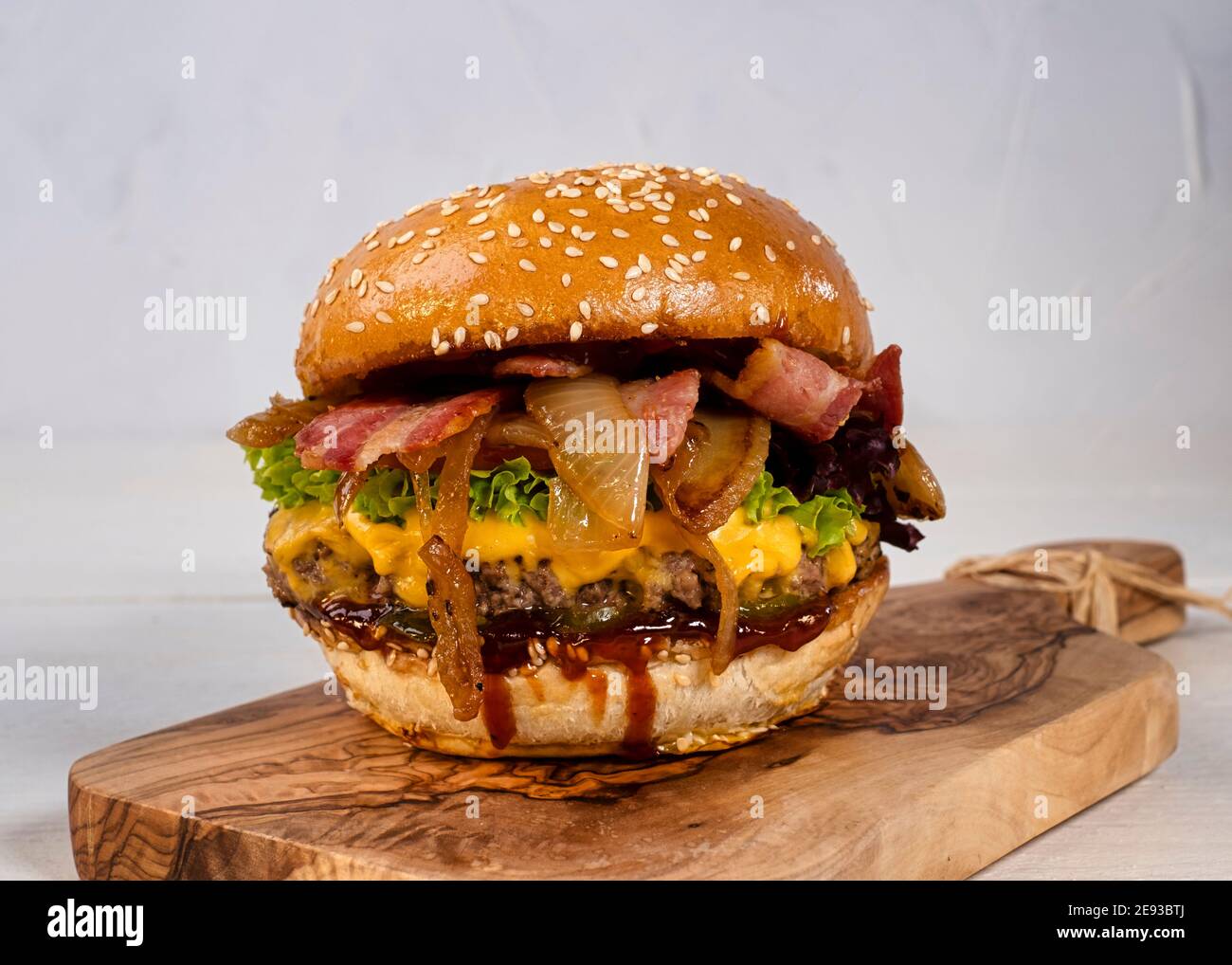 Juicy cheese burger with beef and bacon, tomatoes, cucumbers and onions nicely arranged on a wooden board on a white background Stock Photo