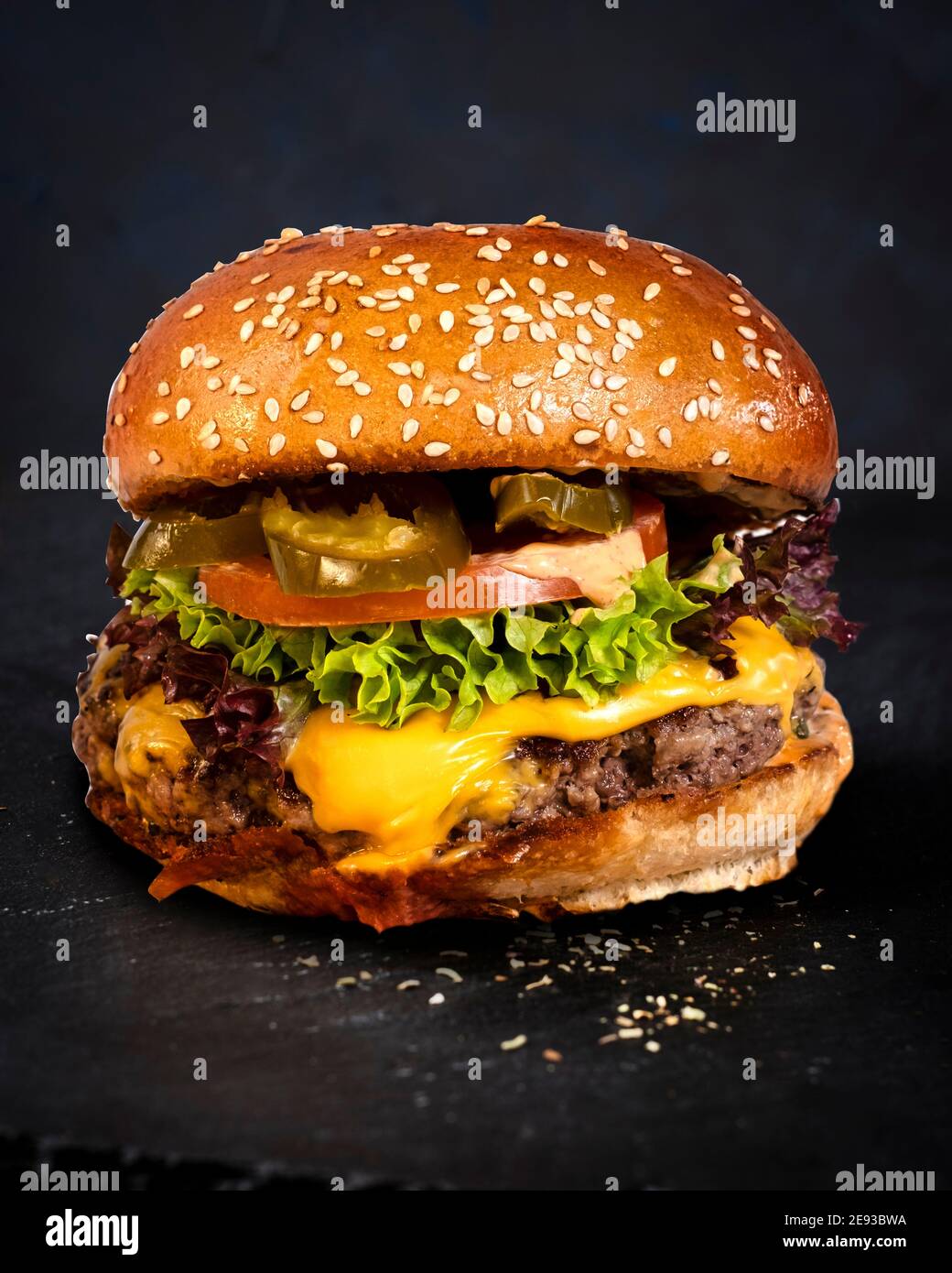 Juicy fiery cheese burger with beef, tomatoes, cucumbers and onions nicely arranged on a skipper plate on a black background Stock Photo